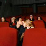 A couple shares a romantic kiss in an empty movie theater, captured from the front.