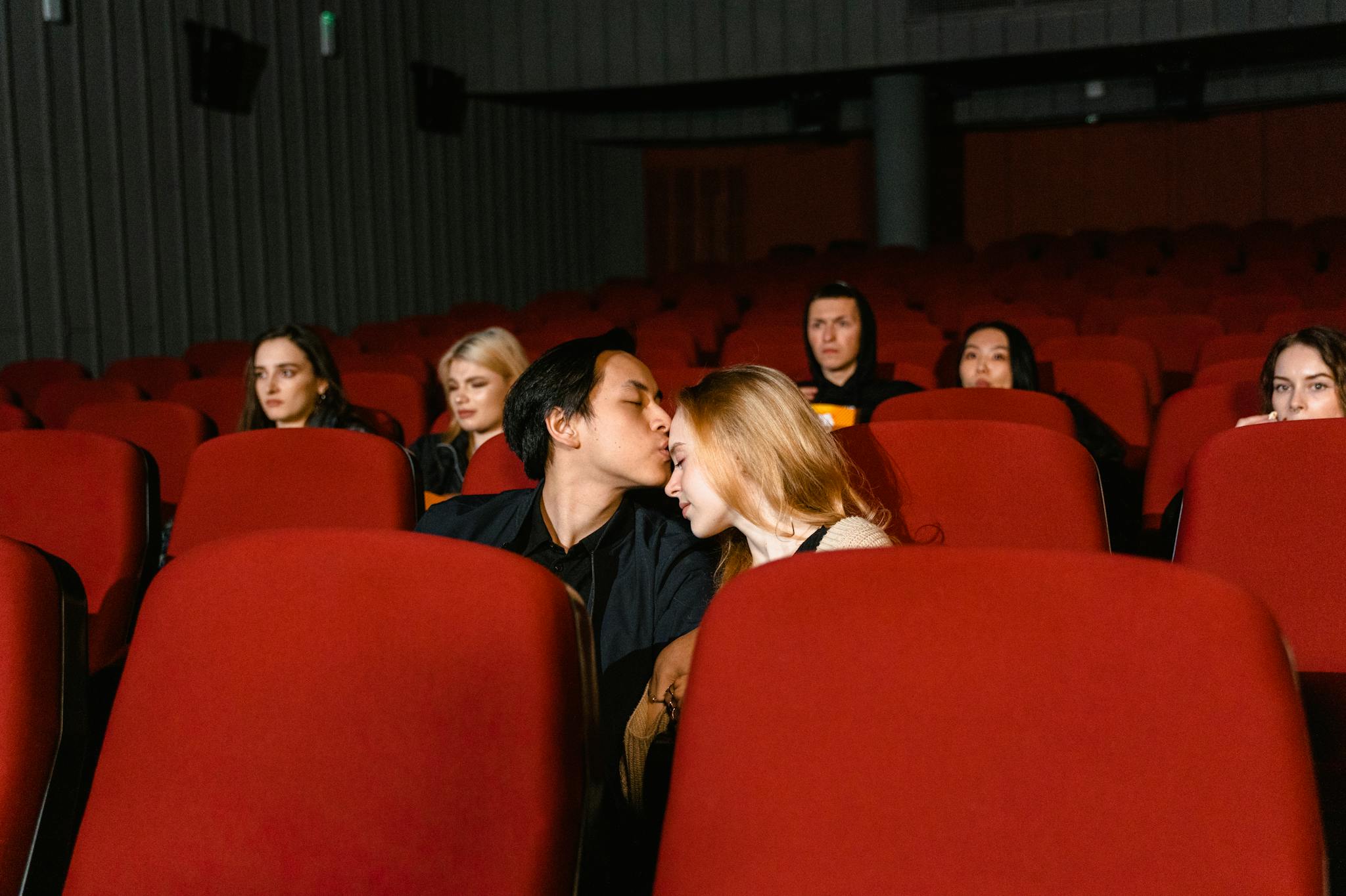 A couple shares a romantic kiss in an empty movie theater, captured from the front.